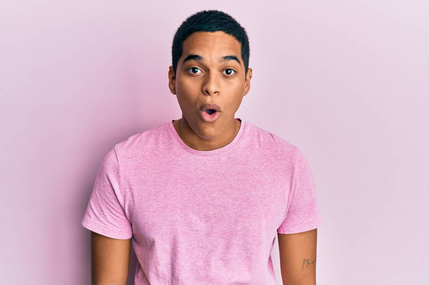 Joven hombre hispano guapo vistiendo camiseta rosa casual asustado y sorprendido con la expresión sorpresa, el miedo y la cara emocionada.  - Foto, imagen