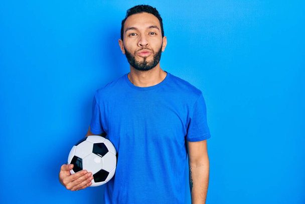 Hispanic man with beard holding soccer ball looking at the camera blowing a kiss on air being lovely and sexy. love expression.  - Photo, Image
