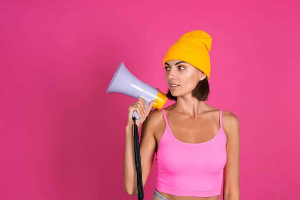 Яркий портрет женщины в жёлтой шляпе на розовом фоне, кричащей в мегафоне - Фото, изображение
