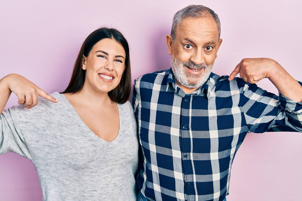 El padre y la hija hispanos vistiendo ropa casual que luce confiada con sonrisa en la cara, señalándose con los dedos orgullosos y felices.  - Foto, imagen