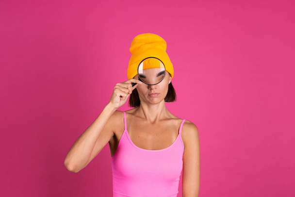 Bright portrait of woman in yellow hat on pink background with magnifier  - Valokuva, kuva