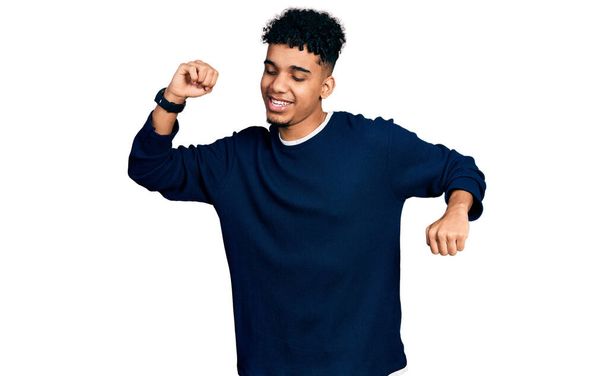 Jeune homme afro-américain portant des vêtements décontractés dansant heureux et joyeux, souriant émouvant occasionnel et confiant écoutant de la musique  - Photo, image