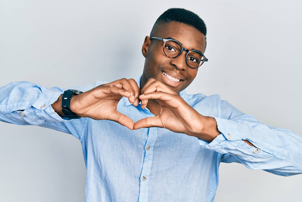Joven hombre afroamericano vistiendo ropa casual y gafas sonriendo en el amor haciendo forma de símbolo del corazón con las manos. concepto romántico.  - Foto, Imagen
