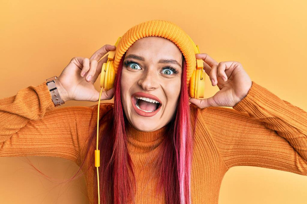Nuori valkoihoinen nainen kuuntelee musiikkia kuulokkeilla juhlii hullu ja hämmästynyt menestystä avoimin silmin huutaen innoissaan.  - Valokuva, kuva