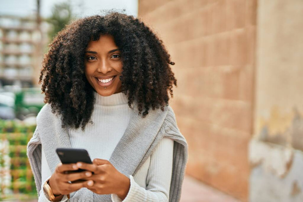 若いアフリカ系アメリカ人の女性が市内のスマートフォンを使って笑顔で. - 写真・画像