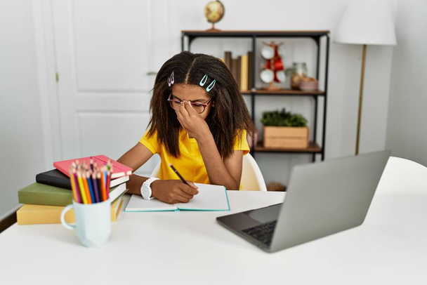 Giovane ragazza afroamericana che fa i compiti a casa stanco sfregamento naso e gli occhi sensazione di stanchezza e mal di testa. concetto di stress e frustrazione.  - Foto, immagini