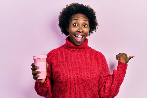 Young african american woman drinking a cup of coffee pointing thumb up to the side smiling happy with open mouth  - Photo, Image