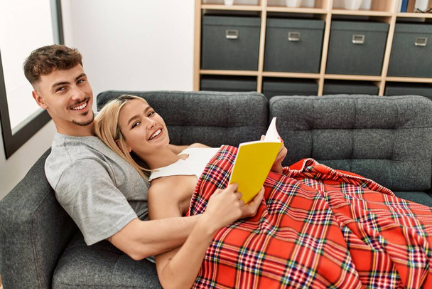 Junges kaukasisches Paar lächelt glücklich Buch zu Hause lesen. - Foto, Bild