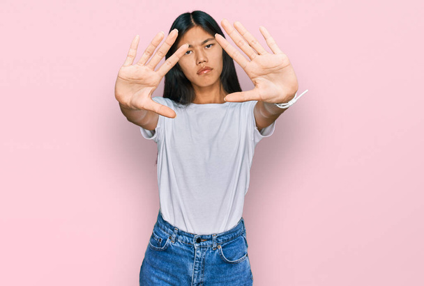 Schöne junge asiatische Frau trägt lässiges weißes T-Shirt dabei Rahmen mit Händen Handflächen und Fingern, Kameraperspektive  - Foto, Bild