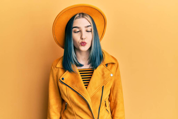 Jeune fille moderne portant chapeau jaune et veste en cuir faisant visage de poisson avec des lèvres, geste fou et comique. expression drôle.  - Photo, image