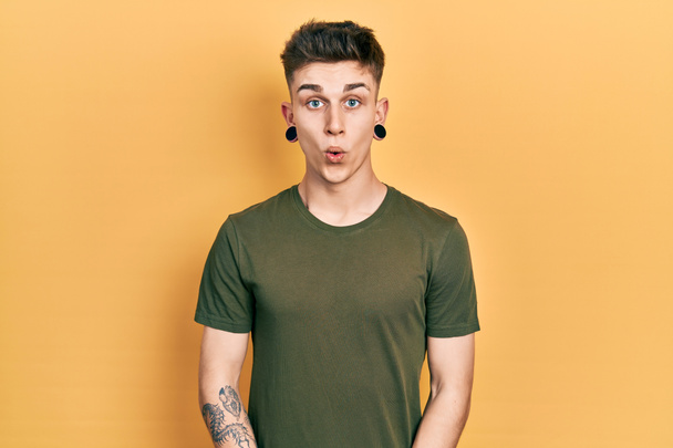 Young caucasian boy with ears dilation wearing casual green t shirt scared and amazed with open mouth for surprise, disbelief face  - Photo, Image