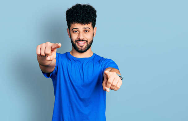Молодой араб с бородой в повседневной синей футболке указывает на тебя и камеру пальцами, улыбаясь позитивно и весело  - Фото, изображение