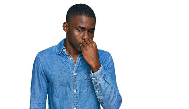 Mladý africký Američan nosí neformální oblečení, vypadá vystresovaně a nervózně s rukama na ústech a kouše nehty. úzkostný problém.  - Fotografie, Obrázek