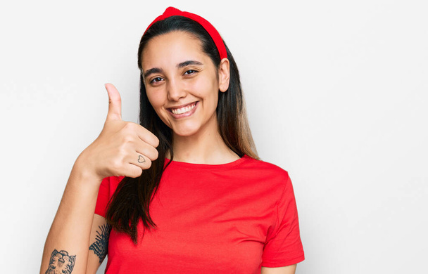 Young hispanic woman wearing casual clothes doing happy thumbs up gesture with hand. approving expression looking at the camera showing success.  - Photo, Image