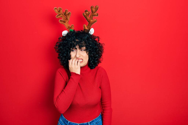 Giovane donna del Medio Oriente che indossa simpatici corna di renna di Natale cercando stressato e nervoso con le mani in bocca mordere le unghie. problema di ansia.  - Foto, immagini