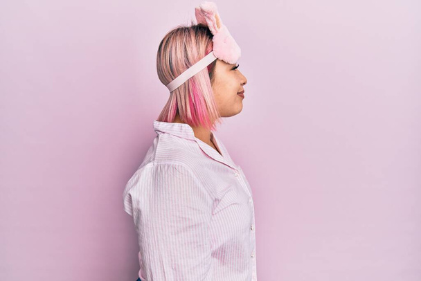 Hispanic woman with pink hair wearing sleep mask and pajama looking to side, relax profile pose with natural face with confident smile.  - Photo, image