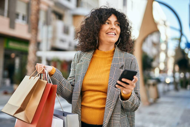 Genç İspanyol kadın alışverişe gidiyor ve şehirde Smatphone kullanıyor.. - Fotoğraf, Görsel