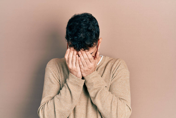 Young hispanic man wearing casual clothes and glasses with sad expression covering face with hands while crying. depression concept.  - Foto, imagen