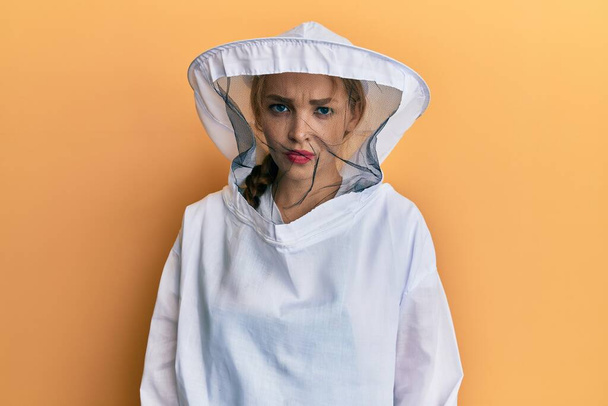 Όμορφη ξανθιά καυκάσια γυναίκα φορώντας προστατευτική στολή μελισσοκόμου σκεπτικός και νευρικός, συνοφρυωμένος αναστατωμένος λόγω του προβλήματος. αρνητικό πρόσωπο.  - Φωτογραφία, εικόνα
