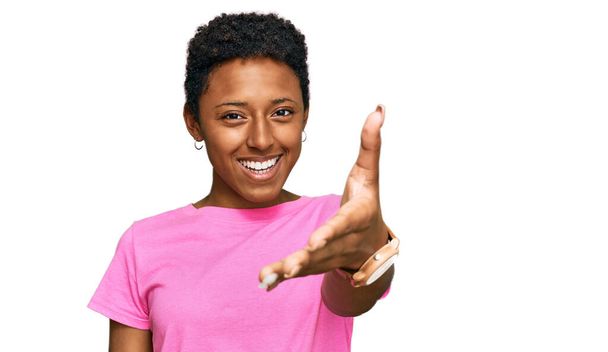 Νεαρή αφροαμερικανή γυναίκα που φοράει καθημερινά ρούχα χαμογελώντας φιλική προσφορά χειραψία ως χαιρετισμό και φιλόξενη. επιτυχημένη επιχείρηση.  - Φωτογραφία, εικόνα