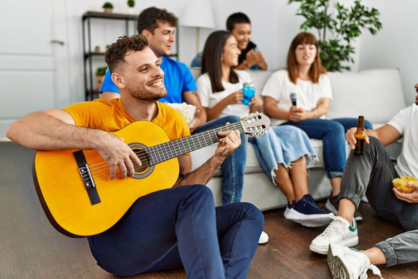 Grupo de jovens amigos na festa sorrindo feliz e tocando guitarra clássica em casa. - Foto, Imagem