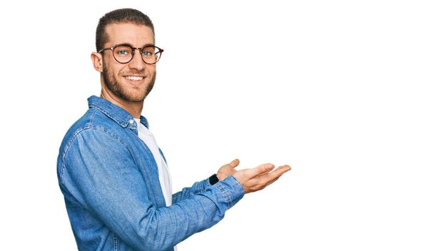 Jonge blanke man draagt casual kleren wijzen opzij met de handen open palmen tonen kopieerruimte, presenteren reclame glimlachend opgewonden blij  - Foto, afbeelding