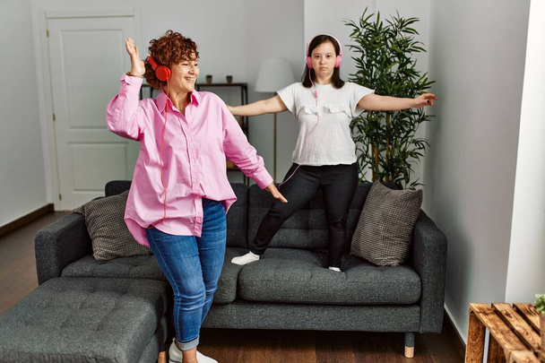 Mature mother and down syndrome daughter at home wearing headphones dancing on the sofa - Foto, Bild