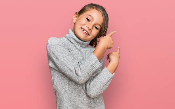 Little beautiful girl wearing casual turtleneck sweater smiling and looking at the camera pointing with two hands and fingers to the side.  - Foto, Imagen