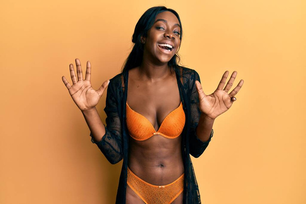 Jovem afro-americana vestindo lingerie mostrando e apontando para cima com os dedos número nove enquanto sorri confiante e feliz.  - Foto, Imagem