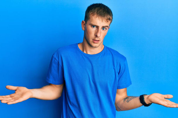 Junger kaukasischer Mann in lässigem blauem T-Shirt ahnungslos und mit offenen Armen verwirrt, keine Ahnung.  - Foto, Bild