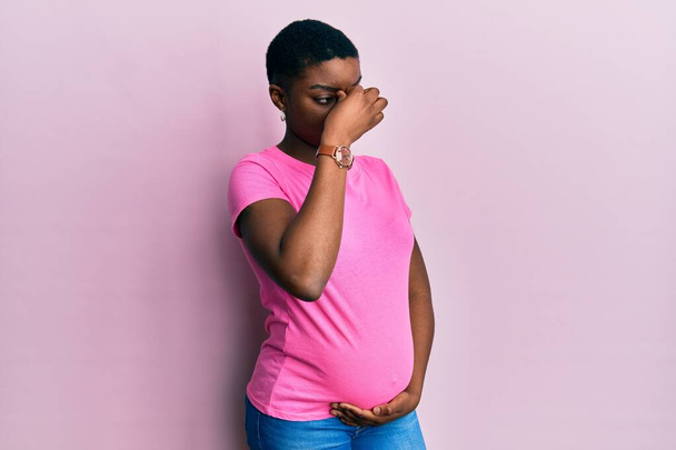 A fiatal afro-amerikai nő gyermeket vár, megérinti a terhes hasat fáradt dörzsölés orr és szemek fáradtság és fejfájás. stressz és frusztráció fogalma.  - Fotó, kép