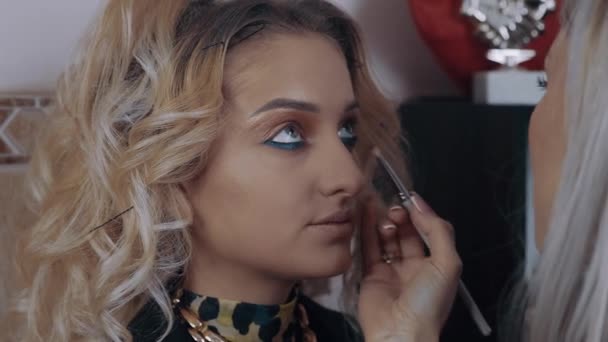 The blonde beautician retouches the skin-colored powder with a toothbrush under her eyes. The process of applying makeup at home by a professional. Artistic concept. - Footage, Video