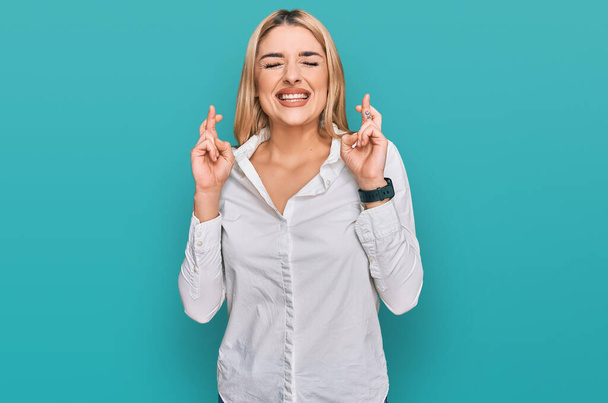 Young caucasian woman wearing casual clothes gesturing finger crossed smiling with hope and eyes closed. luck and superstitious concept.  - Foto, imagen