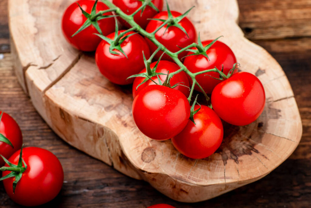 Branch of fresh cherry tomatoes on a brown wooden background. - Foto, afbeelding