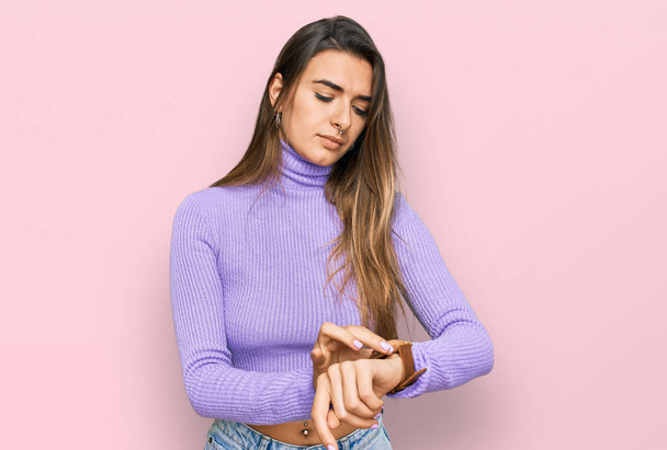 Young hispanic woman wearing casual clothes checking the time on wrist watch, relaxed and confident  - Photo, Image