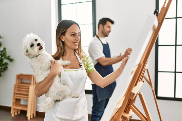 Two hispanic students smiling happy and holding dog painting at art studio. - Foto, immagini
