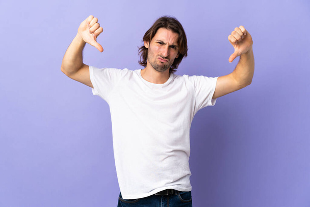 Young handsome man isolated on purple background showing thumb down with two hands - Фото, изображение