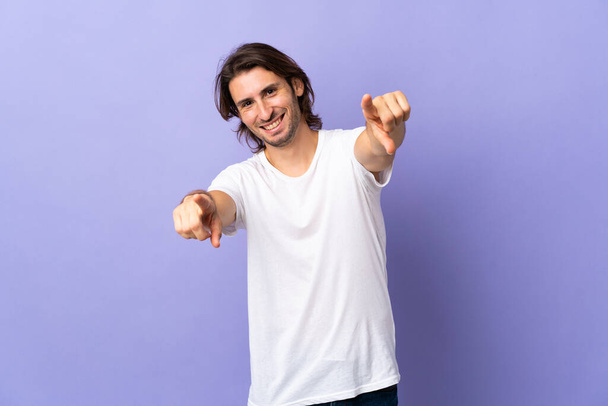Young handsome man isolated on purple background pointing front with happy expression - Photo, Image