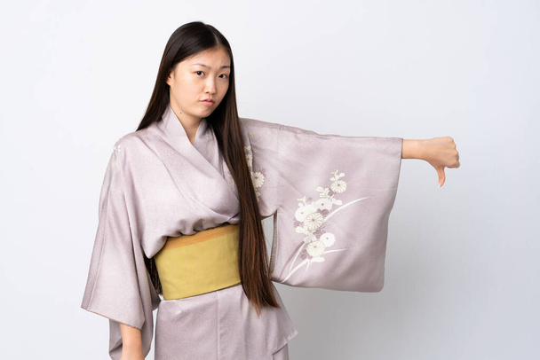 Młoda chińska dziewczyna w kimono na odosobnionym tle pokazuje kciuk w dół z negatywnym wyrazem - Zdjęcie, obraz