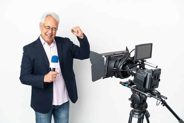 Reportero Hombre brasileño de mediana edad sosteniendo un micrófono y reportando noticias aisladas sobre fondo blanco celebrando una victoria - Foto, Imagen
