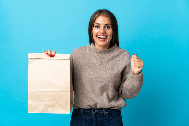 Mavi arka planda bir paket yemek alan bir kadın galibiyeti kutluyor. - Fotoğraf, Görsel