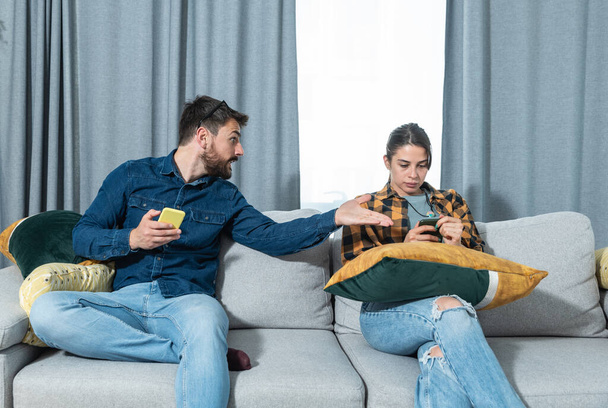 Young couple at home have a problem and argue due to jealousy caused by chatting and flirting via social media networks on smart phones, relationship difficulties problems and distrust - Photo, Image