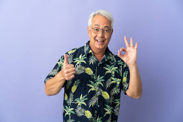 Middle age Brazilian man isolated on purple background showing ok sign and thumb up gesture - 写真・画像