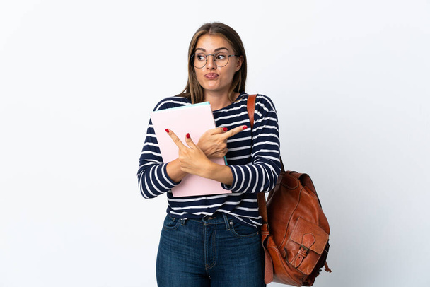 jonge student vrouw geïsoleerd op witte achtergrond wijzend naar de lateralen met twijfels - Foto, afbeelding