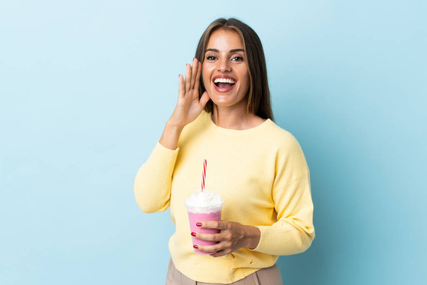 Young Uruguayan woman with strawberry milkshake isolated on blue background shouting with mouth wide open - Foto, imagen