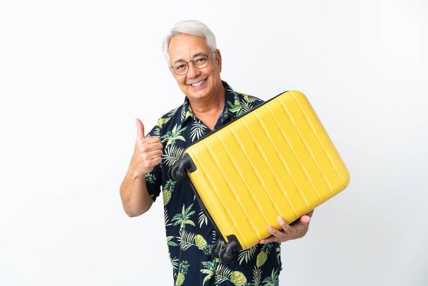 Hombre brasileño de mediana edad aislado sobre fondo blanco en vacaciones con maleta de viaje y con pulgar hacia arriba - Foto, imagen