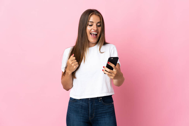 Young Uruguayan woman isolated on pink background with phone in victory position - Fotografie, Obrázek