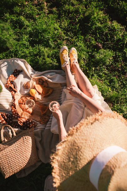 mujer piernas en manta teniendo picnic en la puesta del sol alimentos bebida al aire libre verano - Foto, Imagen