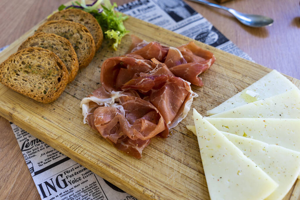 A closeup of a dinner table covered with bacon, cheese, bread on a wooden board. - 写真・画像