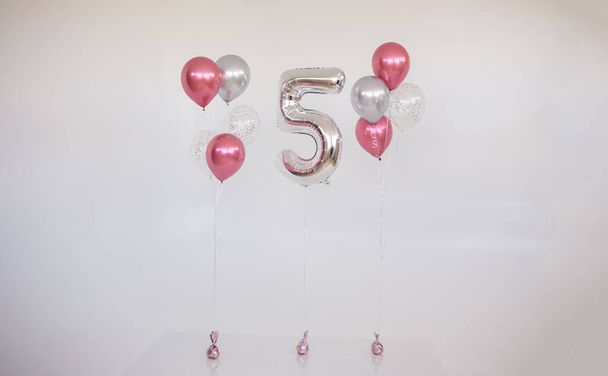 μια σειρά από ροζ μπαλόνια με ήλιο και ένα φουσκωτό αριθμό πέντε σε λευκό φόντο με μια θέση για κείμενο - Φωτογραφία, εικόνα